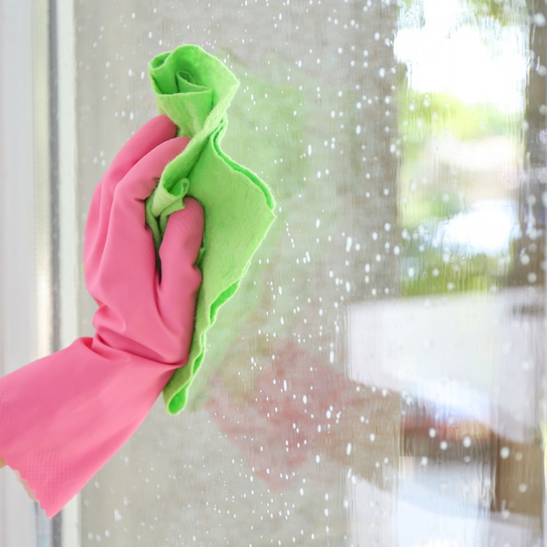 Persons hand with a pink glove on cleaning a window