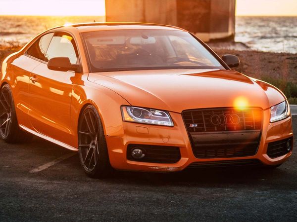 An orange Audi S5 parked by the ocean