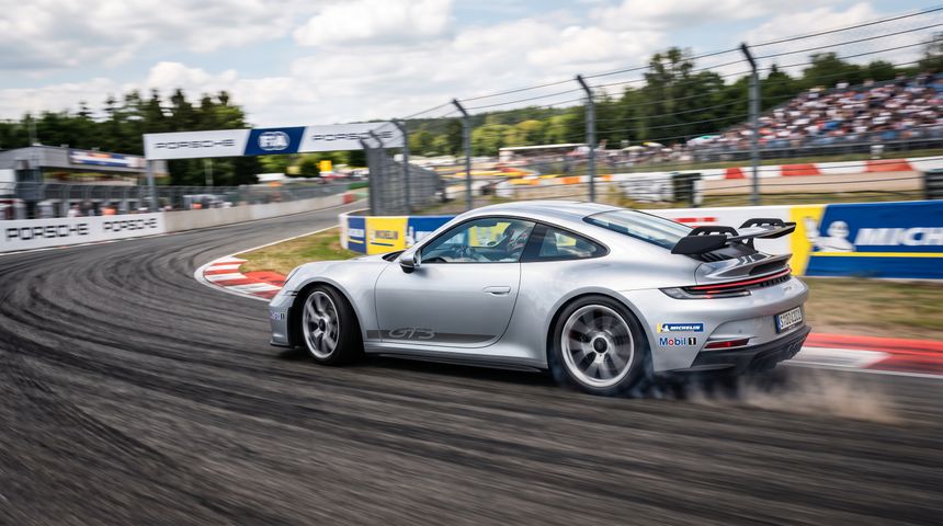 A grey sports car speeds around a corner on an asphalt race track during a sunny track day.