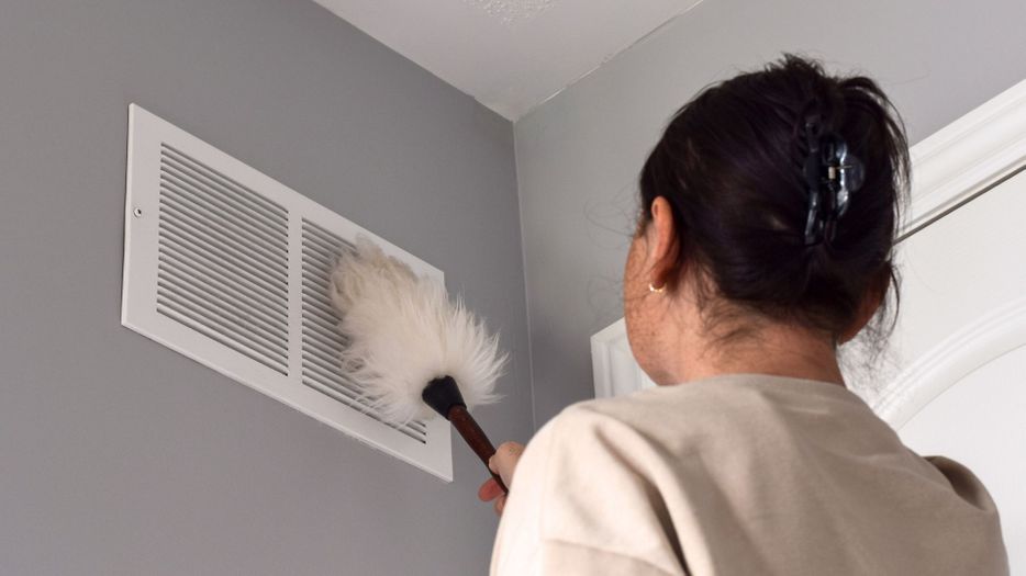 Person dusting a home air vent on the wall