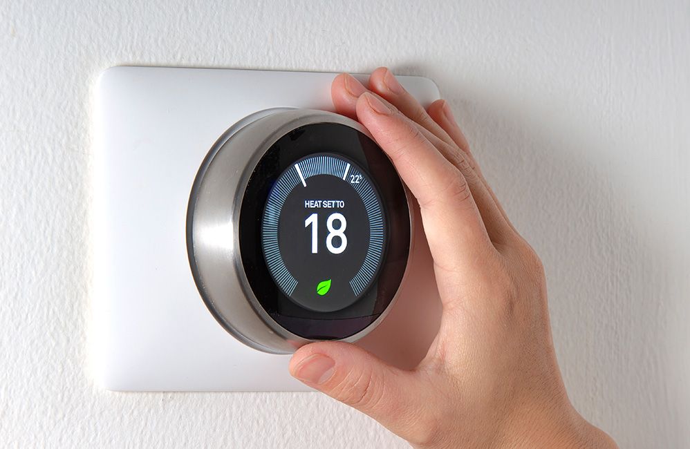 A hand adjusting a wall-mounted smart thermostat
