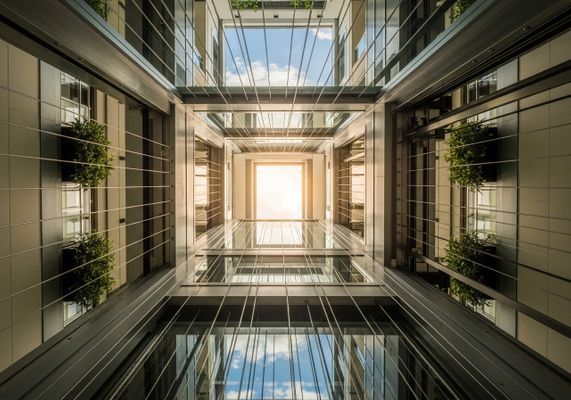 Modern glass elevator shaft in a commercial building representing professional elevator maintenance services. Modern glass elevator shaft in a commercial building representing professional elevator maintenance services.