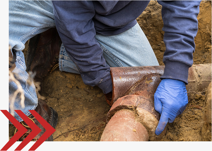 Man working on a sewer line in the dirt. 