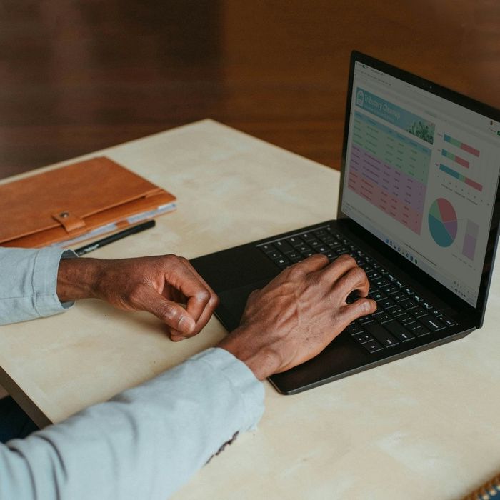 A close-up shot of a person typing on a laptop with charts and data displayed on the screen, indicating work or a business task.