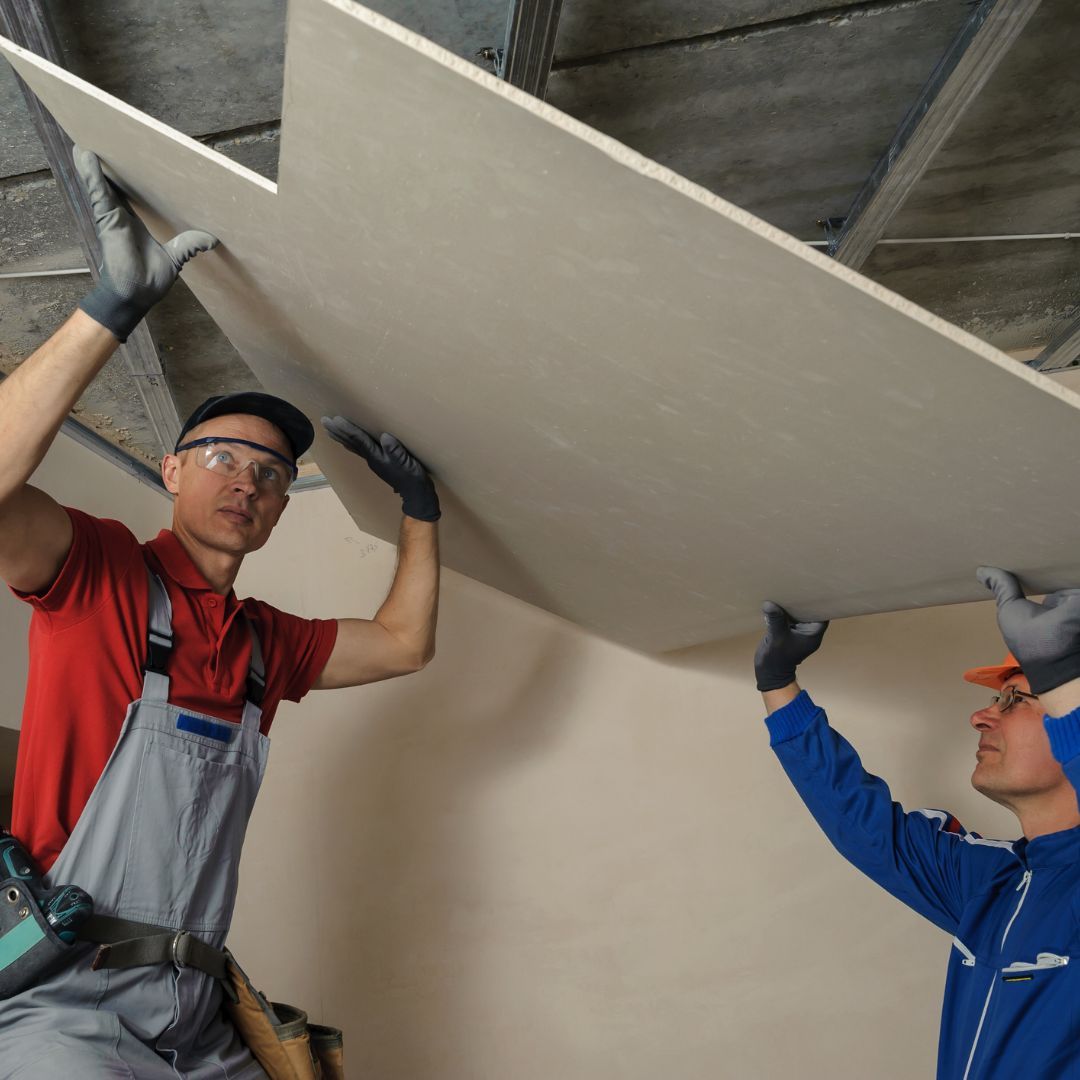 Two men putting drywall sheets up on roof 