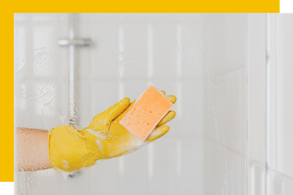 person wiping down shower glass with a sponge. 