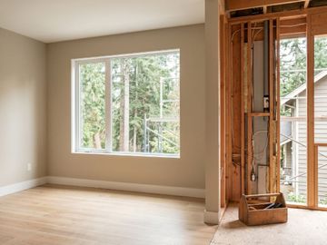 A master bedroom suite addition in progress showing finished hardwood floors next to open wall studs with insulation and wiring.