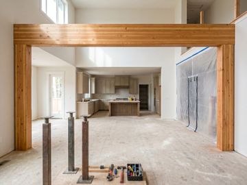A large structural glulam wood beam and support posts framing a wide, open-concept kitchen remodel with protective dust walls.