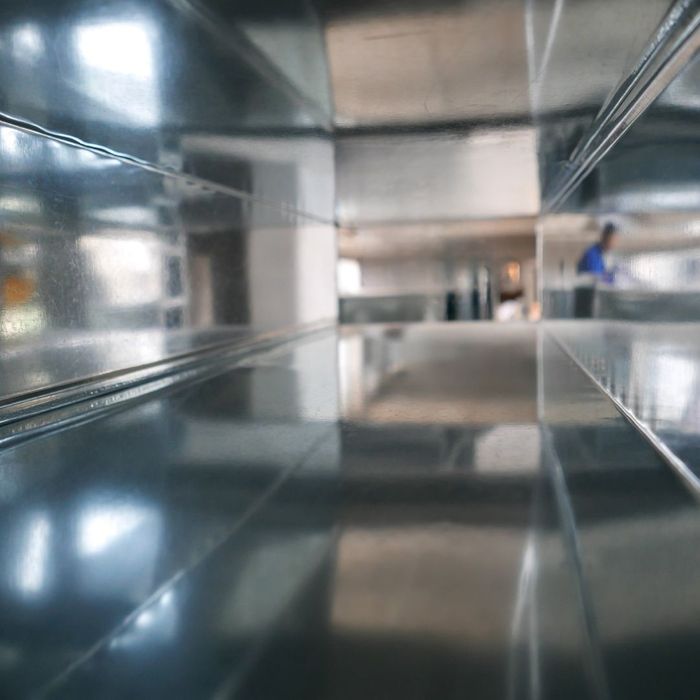 Interior view of a large, empty, metallic duct system with a blurry figure in blue working in the distance.