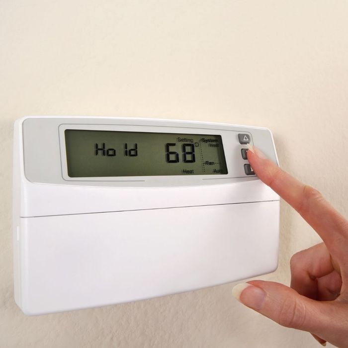 A close-up shot of a person’s finger adjusting the temperature settings on a white digital wall thermostat displaying 68 degrees.