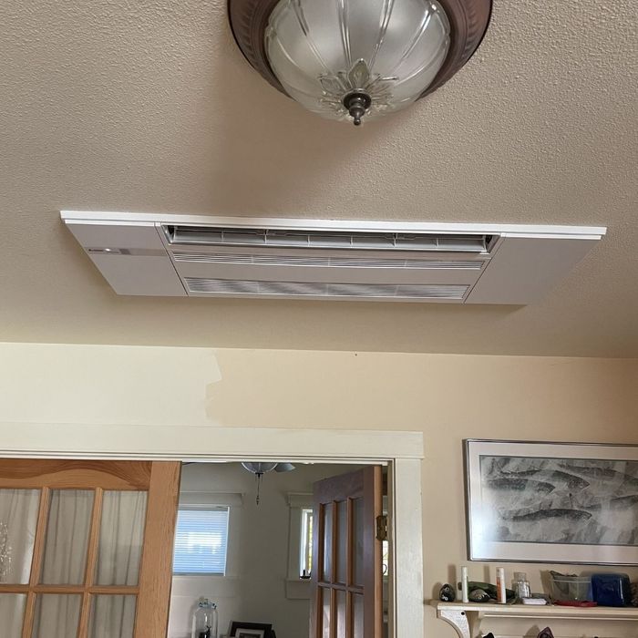 A clean, white ceiling-mounted ductless air conditioning unit installed in a home with neutral-toned walls and traditional decor.