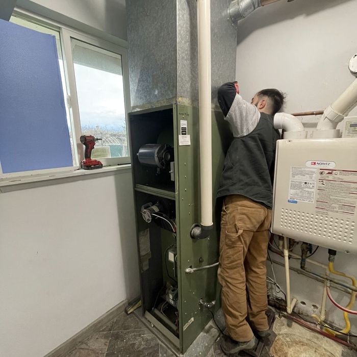 A person works on a furnace with the access panel open, next to a water heater.