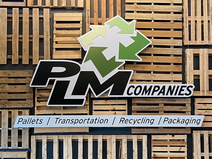 PLM Companies brand logo on a wall of repurposed pallets. 