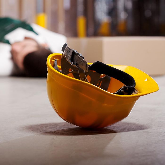 Yellow hardhat on the ground with an injured warehouse worker in the background