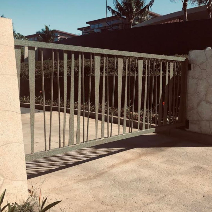 Gray metal gate casting shadows on concrete driveway.