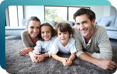 Happy family with 2 kids smiling while laying on clean carpet in living room