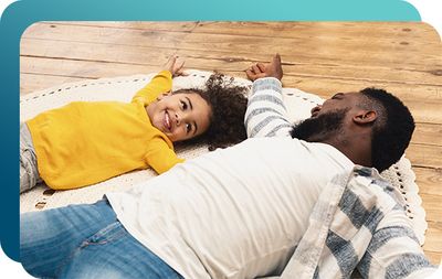 Smiling young girl laying on rug on hardwood floor with her dad