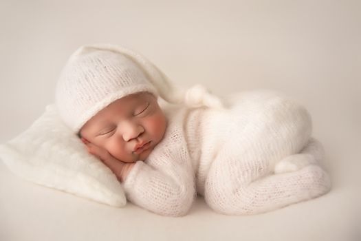 Newborn baby sleeping in a white outfit and bonnet on cream background, photographed by Kelly Saxon Photography, professional newborn photographer on Murfreesboro, Tennessee Whote Newborn Studio Portrait - Kelly Saxon Photography