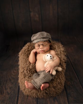Newborn baby boy wearing a hat and glasses while holding a teddy bear, captured by Kelly Saxon Photography, professional newborn photographer in Murfreesboro, Tennessee. Newborn Boy Photo with Teddy Bear - Kelly Saxon Photography