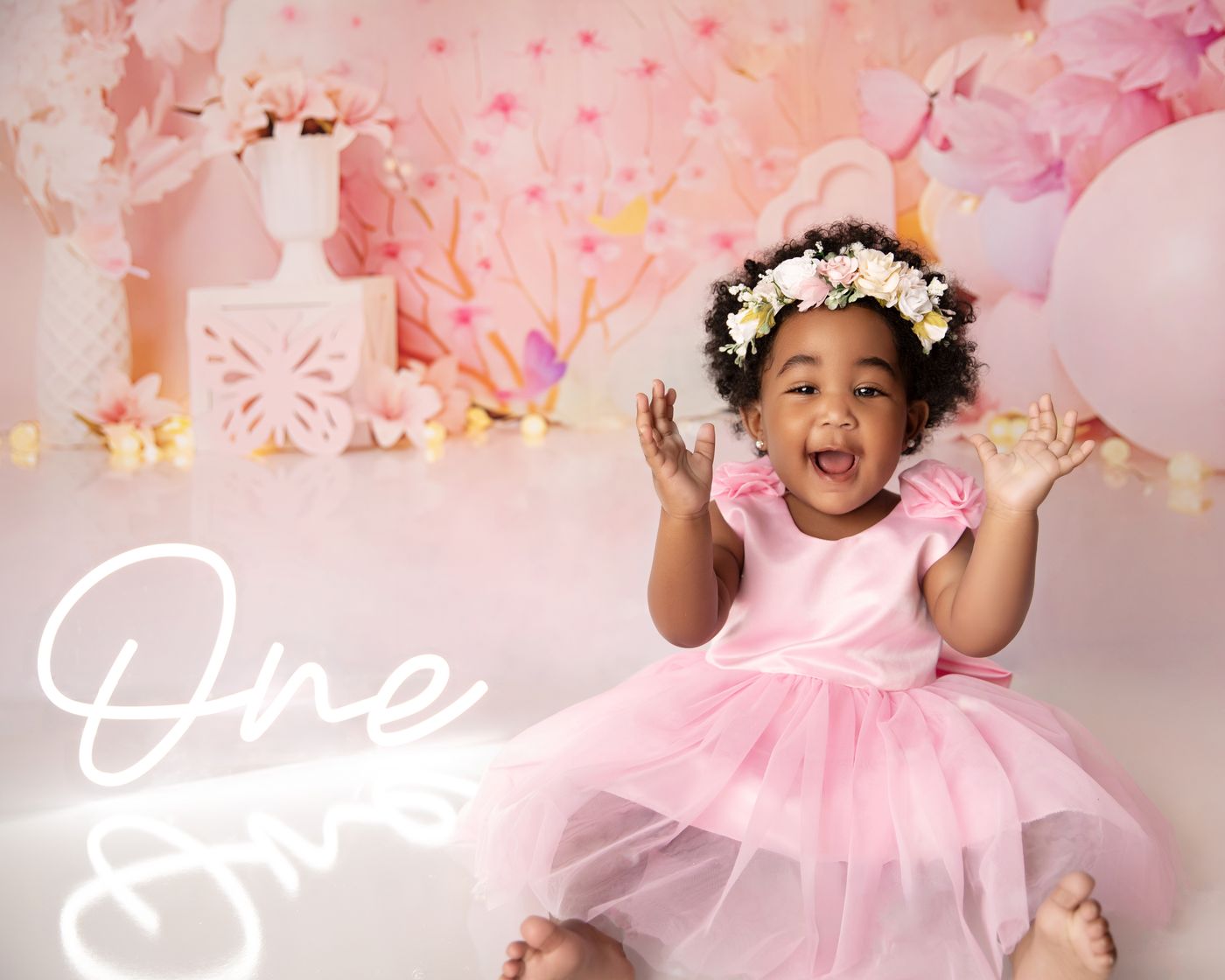 Smiling baby girl in a pink fress and floral headbabnf during a styled milestone photography session near Murfreesboro, Tennessee. Baby Cake Smash Photographer Murfreesboro TN | Kelly Saxon Photography