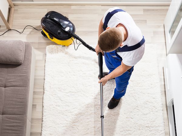 A man cleans his apartment’s carpet rug.