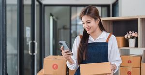 woman in business looks at phone while preparing deliveries How To Prepare Your Books for Tax Season.jpg