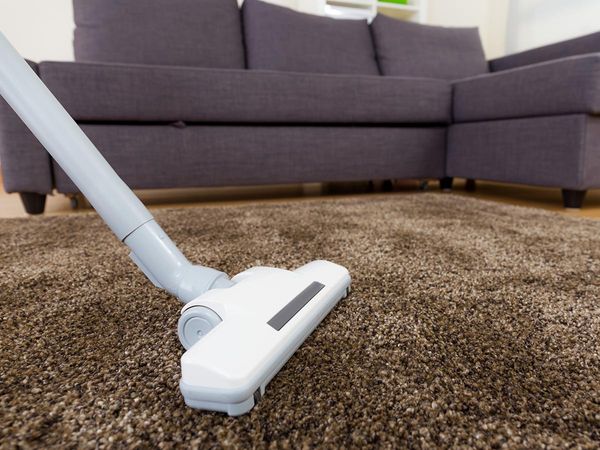 Person vacuuming carpet next to a sofa
