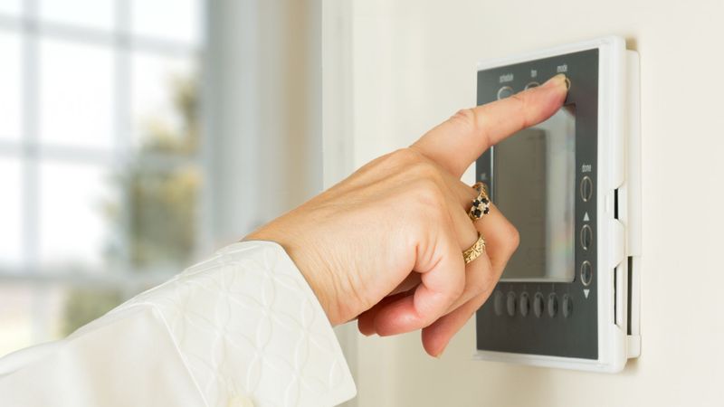 Image of a woman adjusting a thermostat