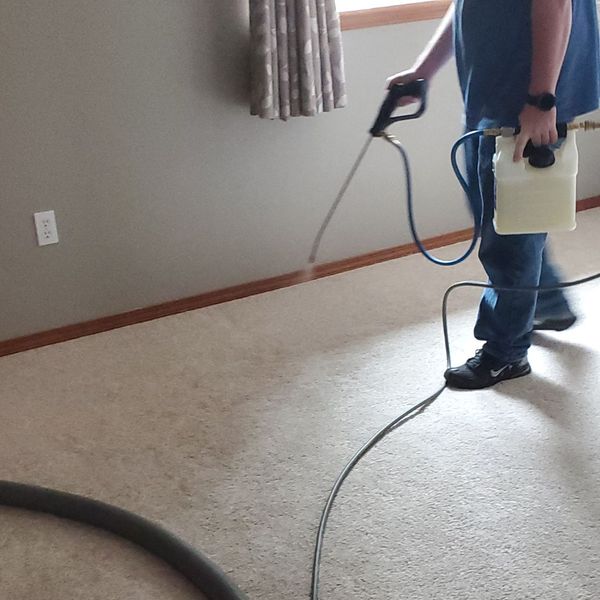 A technician carefully applies a specialized cleaning treatment along the edges and baseboards of a room.