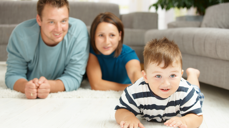 parents watching their child crawl across the floor. 