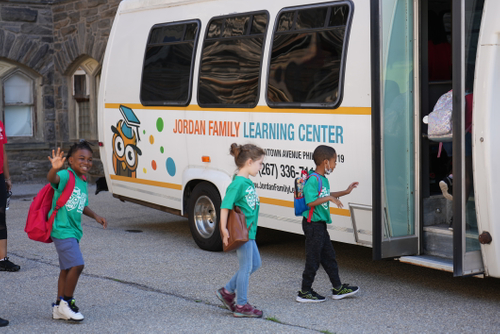 kids waving as they enter a bus