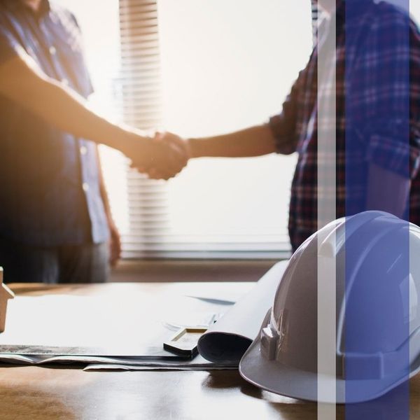 Contractors shaking hands with hard hat in the foreground