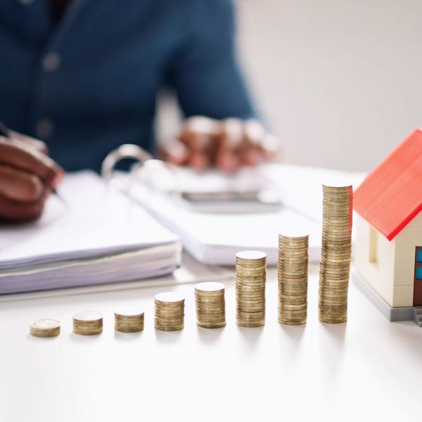 Person crunching numbers with coins and small house in front of them