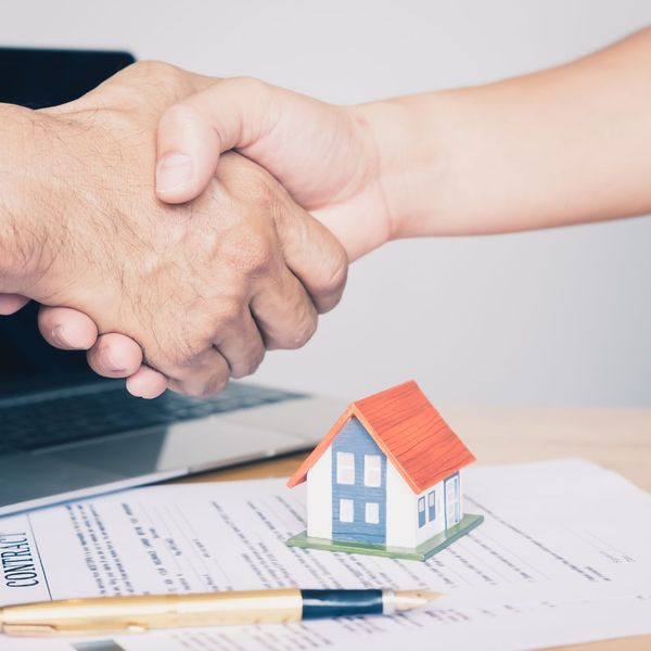 People shaking hands with house and contract under them