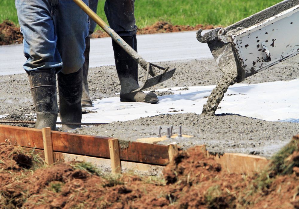 concrete being poured with workers standing and spreading the mixture