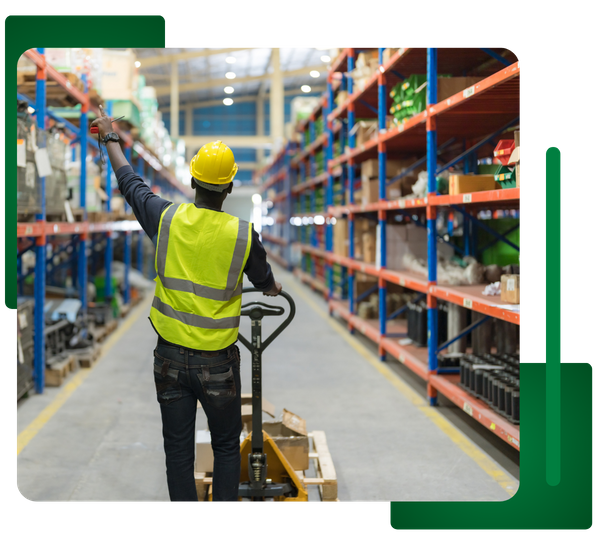 Worker in safety vest/helmet operating a pallet jack in a warehouse aisle.