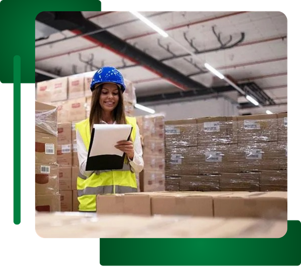 Woman in safety vest/helmet checking inventory in a warehouse with bright ceiling lighting.