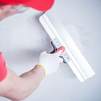 a worker smoothing putty on drywall
