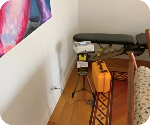 Radon testing equipment set up on a tripod with an orange case in a room corner.