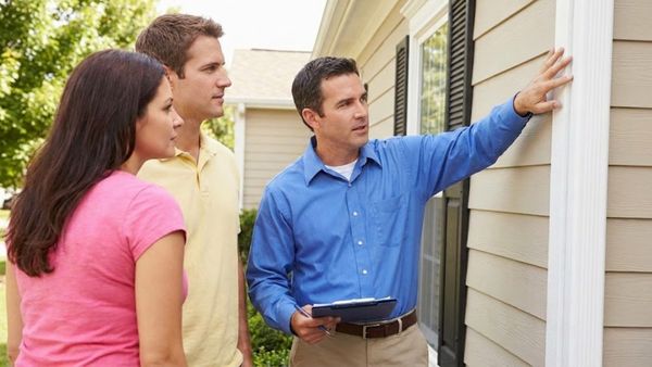 A home inspector shows a couple a detail on the exterior of a house.