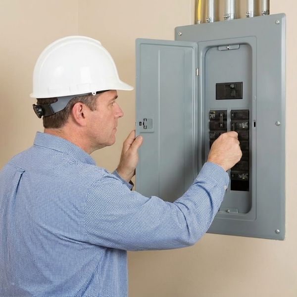 A home inspector in a hard hat examines an open electrical panel.