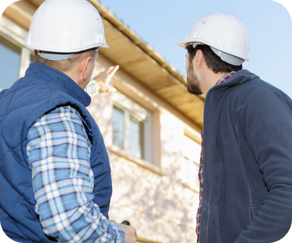 Two construction workers in hard hats looking up and pointing at a building's exterior.