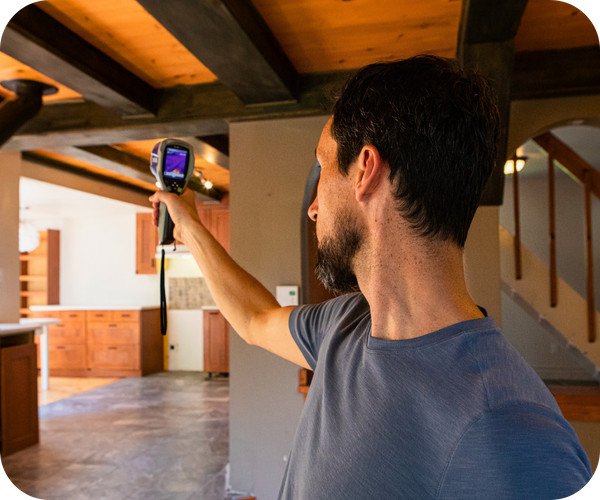Man using a thermal imaging camera to inspect an interior wall of a house. Man using a thermal imaging camera to inspect an interior wall of a house.