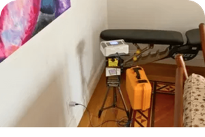 Radon testing equipment set up on a tripod in a room corner, next to a wall outlet.