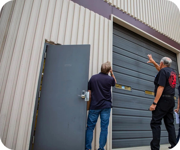 Two men inspecting a large commercial garage door and a side entrance.
