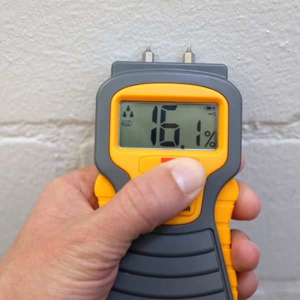 A gloved hand uses a moisture meter to check a wall for dampness.