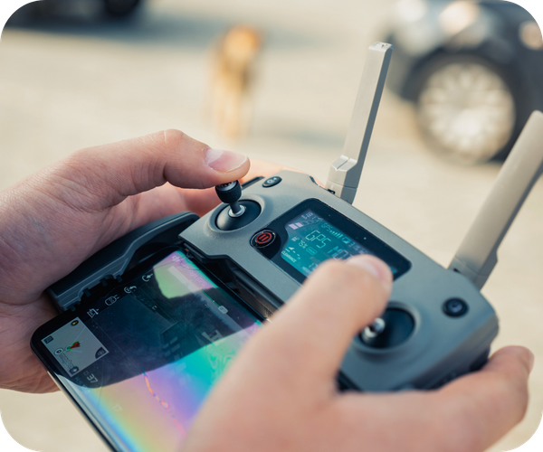 Hands operating a drone controller with a smartphone displaying a live feed, used for roof inspections. Hands operating a drone controller with a smartphone displaying a live feed, used for roof inspections.