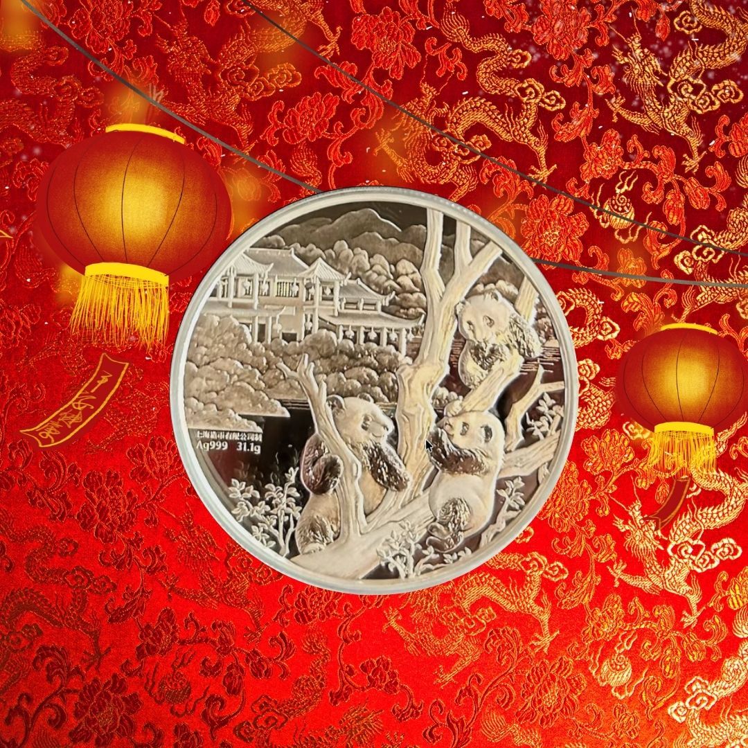 silver bullion coin featuring three pandas in a forest setting, centered against a vibrant red silk background embossed with golden dragon and floral patterns. Two glowing red paper lanterns with gold tassels hang on either side of the coin.