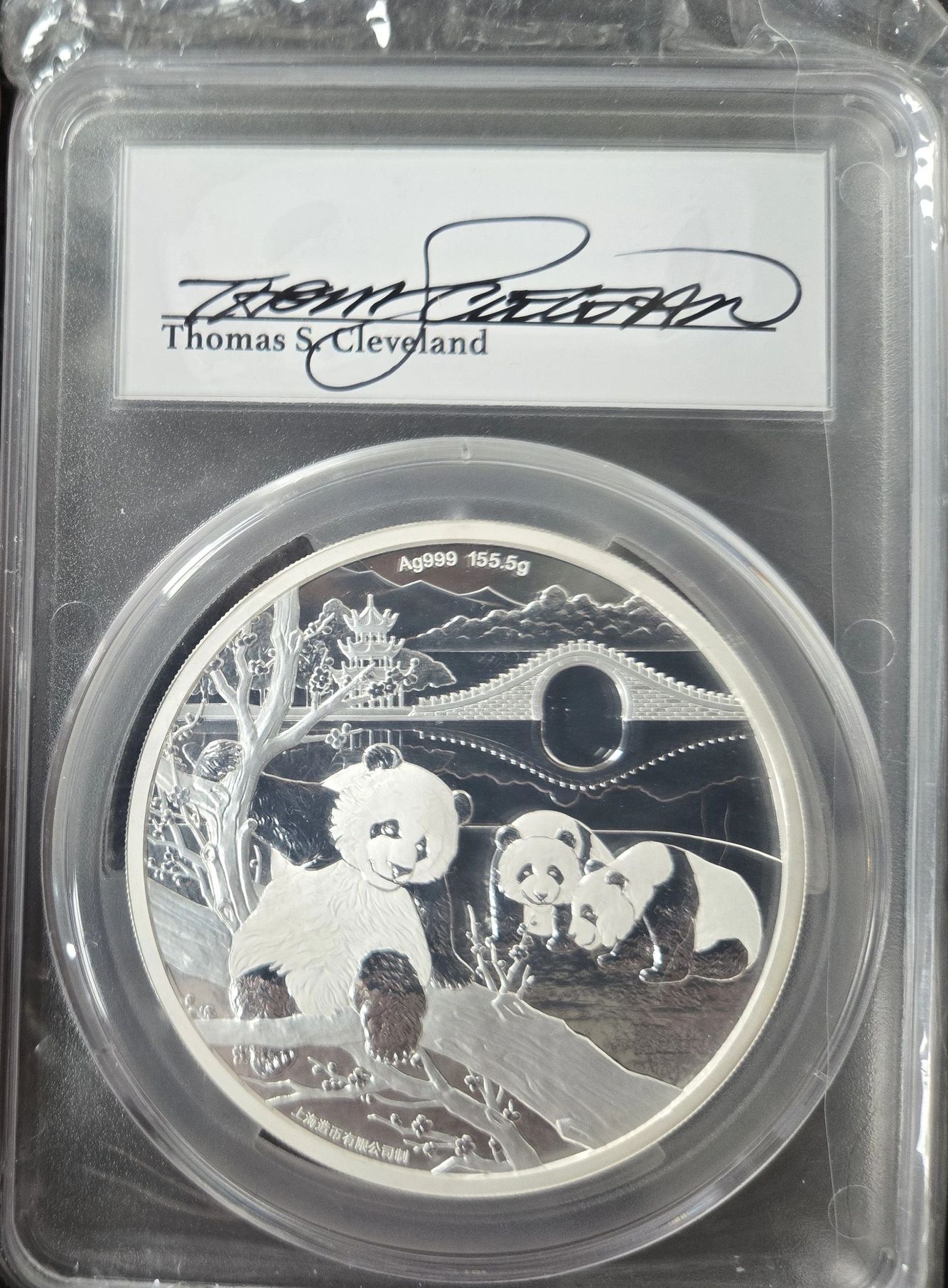 A professional numismatic grading slab containing a large 155.5g Ag999 silver coin. The label features the signature of "Thomas S. Cleveland". The coin's design depicts three pandas in a landscape with a moon bridge and pagoda.