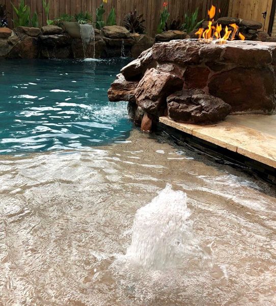 Bubbler and rock waterfall running on a Houston pool with a fire feature above